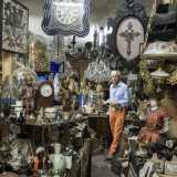 Seguiamo l�antiquario lungo un corridoio strettissimo che conduce al retro bottega. Da una parte e dall�altra non possiamo fare a meno di notare antichi specchi, piccolissimi giocattoli degli anni 40, lampade ad olio...